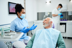 Happy senior man talking to black female dentist during appointment at general dental services appointment